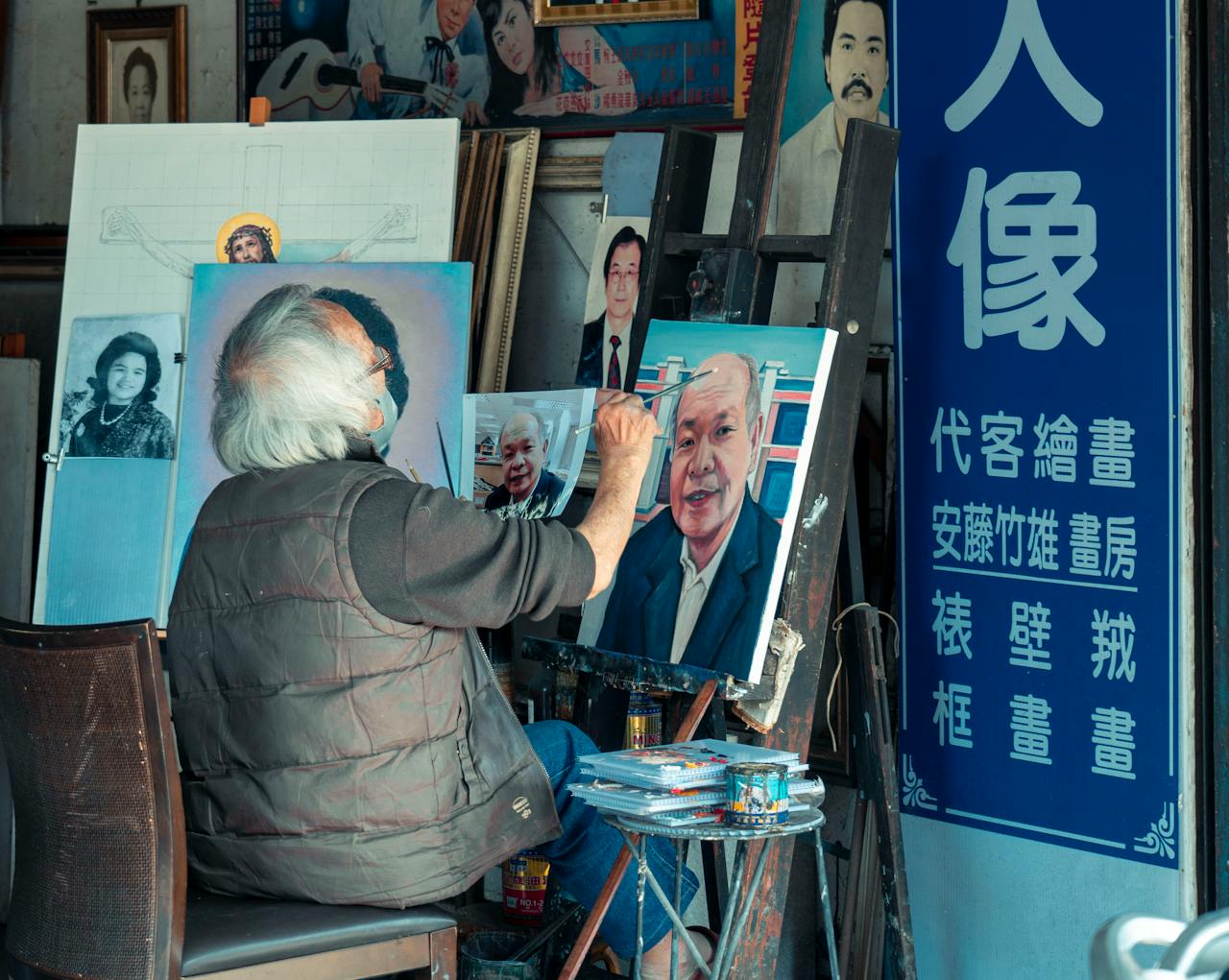 Senior artist captures portraits in a creative studio, surrounded by artwork and tools of his trade.