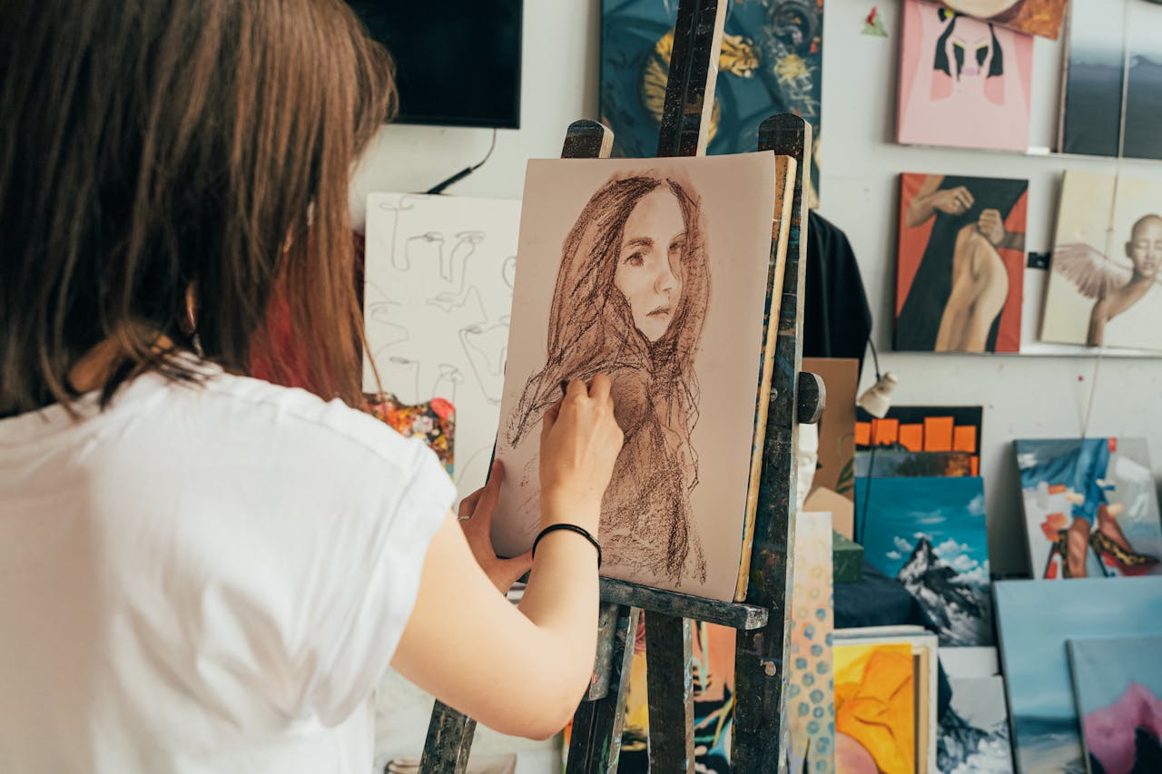 Woman drawing in an art studio surrounded by finished paintings and artworks.